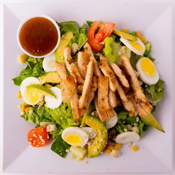 A Bowl of Greens salad with grilled chicken, avocado, hard-boiled eggs, and dressing.