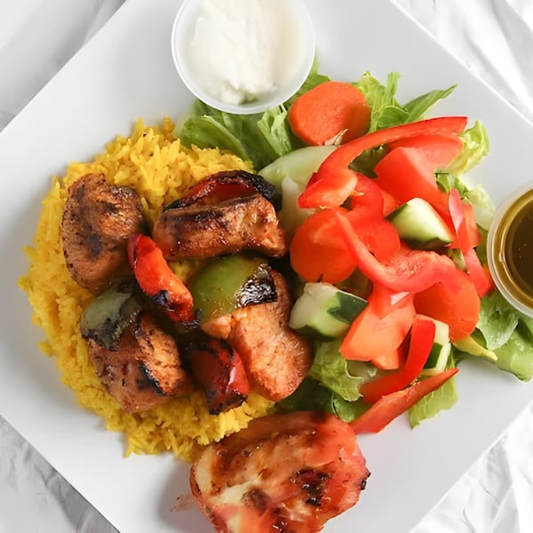 Grilled chicken and vegetable skewers with yellow rice, a side salad, and two dressings.
