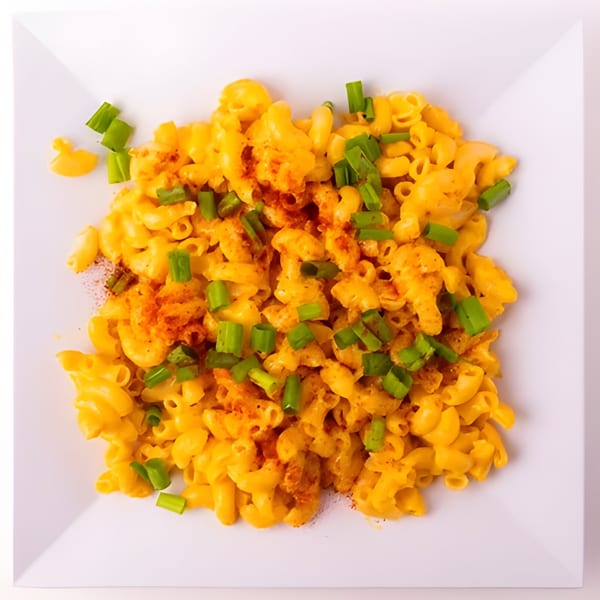 Macaroni and cheese with green onions and paprika on a white square plate.