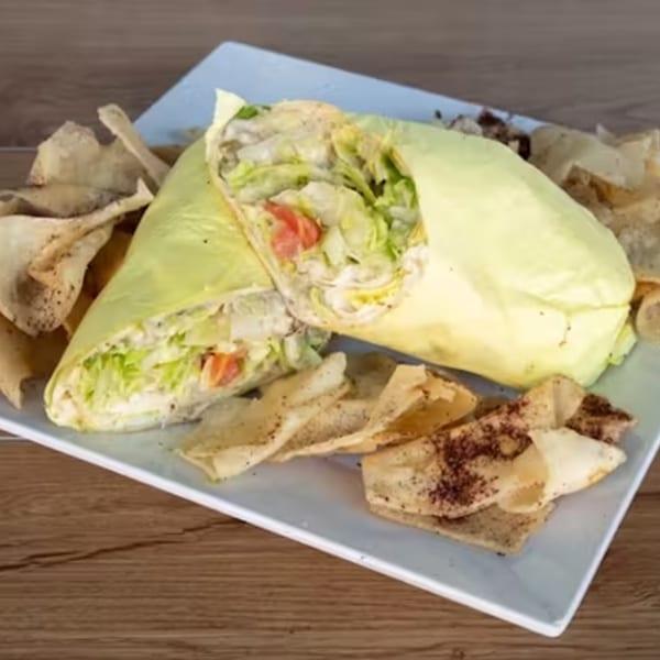 Two salad wraps filled with lettuce and tomatoes, served with seasoned pita chips on a white plate.